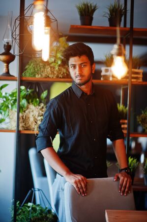 Confident young indian man in black shirt standing at cafe.