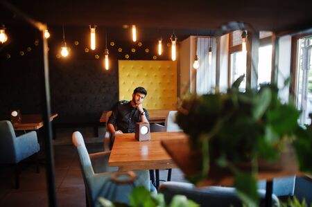 Confident young indian man in black shirt sitting at cafe.の写真素材