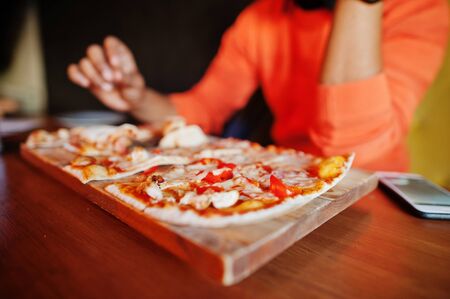 Close up hand of man in orange sweater sitting at pizzeria with pizza.の写真素材