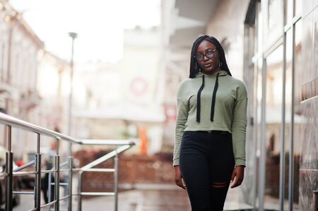 City portrait of positive young dark skinned female wearing green hoody and eyeglasses.の写真素材