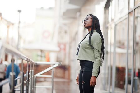City portrait of positive young dark skinned female wearing green hoody and eyeglasses.の写真素材