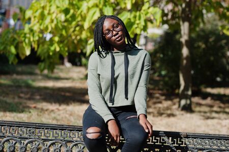 City portrait of positive young dark skinned female wearing green hoody and eyeglasses.