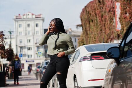 City portrait of positive young dark skinned female wearing green hoody and eyeglasses walking at...
