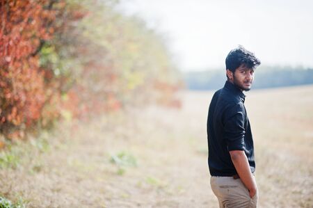Indian man at black shirt and beige pants posed at field against autumn leaves.