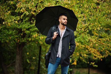 Fashionable tall arab beard man wear on black coat with umbrella and bag case posed at rain weather day.の写真素材
