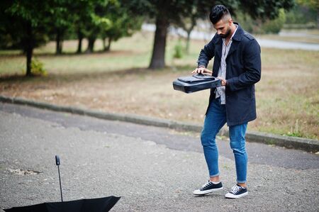 Fashionable tall arab beard man wear on black coat with umbrella and bag case posed at rain weather day.の写真素材