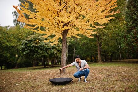 Fashionable tall arab beard man wear on shirt, jeans and sunglasses posed on autumn park with umbrella against yellow leaves tree.の写真素材