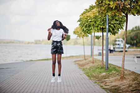 African american dark skinned slim model posed in a black leather shorts and white t-shirt. She jumping at the air.の写真素材