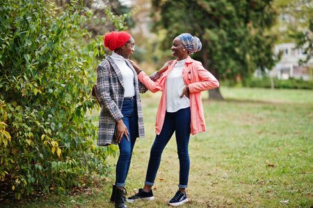 Two young modern fashionable, attractive, tall and slim african muslim womans in hijab or turban head scarf and coat posed at park together.の写真素材
