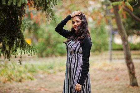 Portrait of young beautiful indian or south asian teenage girl in dress posed at autumn park in...