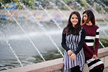 Portrait of two young beautiful indian or south asian teenage girls in dress posed against fountains.の写真素材