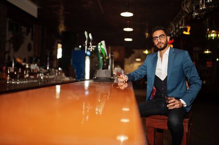 Handsome well-dressed arabian man with glass of whiskey and cigar posed at pub.の写真素材