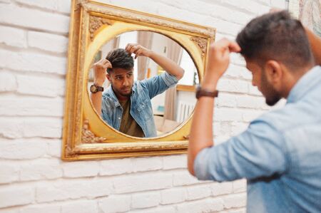 Portrait of handsome successful bearded south asian, young indian freelancer in blue jeans shirt standing in cafe and look at mirror.の写真素材
