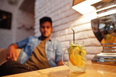 Portrait of handsome successful bearded south asian, young indian freelancer in blue jeans shirt sitting in cafe with lemonade.の写真素材