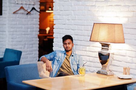 Portrait of handsome successful bearded south asian, young indian freelancer in blue jeans shirt sitting in cafe with lemonade.の写真素材