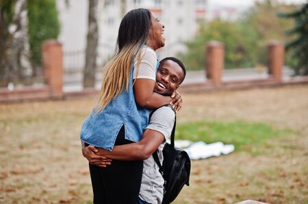 Two african students with backpack on yard of university hugs and having fun together.