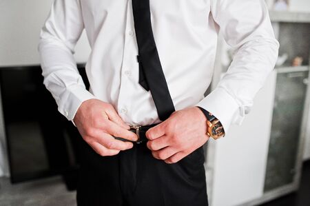 Morning of the groom preparation. Young and handsome groom getting dressed. Tie belt.の写真素材