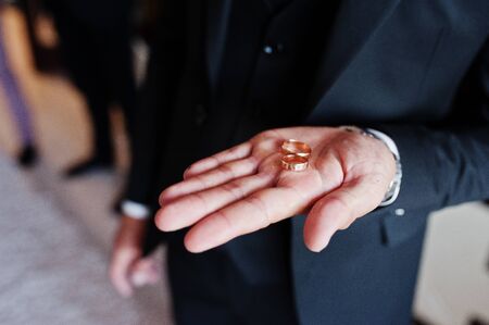 Morning of the groom preparation. Young and handsome groom hold wedding rings on hand.の写真素材