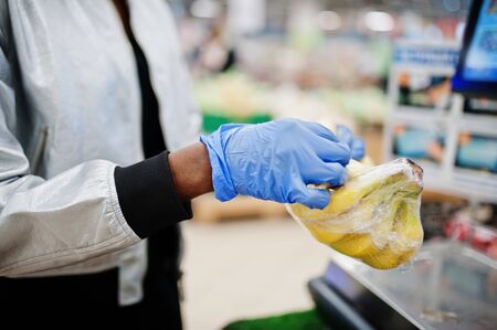 African woman wearing disposable medical mask and gloves shopping in supermarket during coronavirus...
