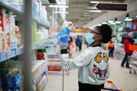 African woman wearing disposable medical mask and gloves shopping in supermarket during coronavirus...