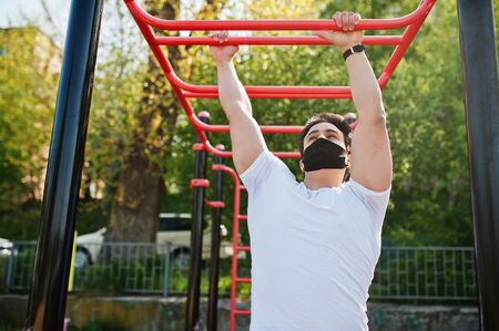 Portrait sports arabian man in black medical face mask doing workout exercises in outdoor gym place...