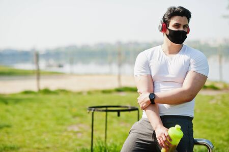 Portrait sports arabian man in black medical face mask posed outdoor with earphones during coronavirus quarantine.の写真素材