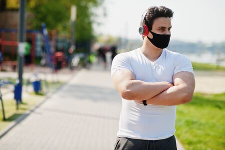 Portrait sports arabian man in black medical face mask posed outdoor with earphones during coronavirus quarantine.の写真素材