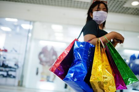 African american woman wearing face protective medical mask for protection from virus disease with shopping bags in mall during coronavirus pandemia.の写真素材