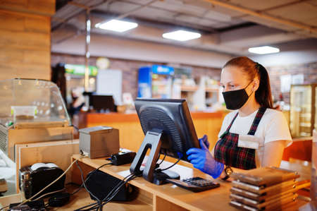 Waiter in protective mask in the restaurant at counter with cashbox working at bar.
