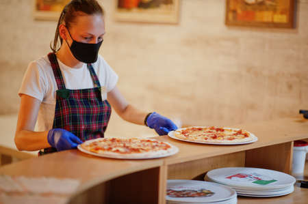 Waiter in protective mask hold pizza in pizzeria.の写真素材