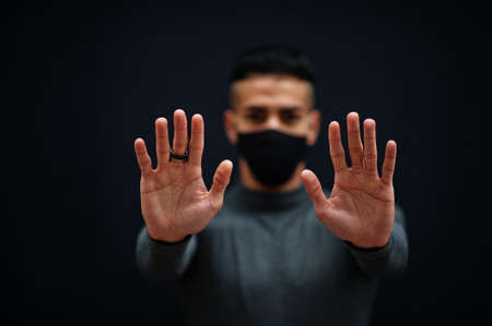 Middle eastern man in gray turtleneck and black face protect mask on isolated background show two hands, stop sign.の写真素材