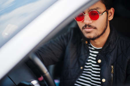 South asian man or indian male wear red eyeglasses sitting inside his white transportation car.
