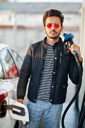 South asian man or indian male refueling his white car on gas station.