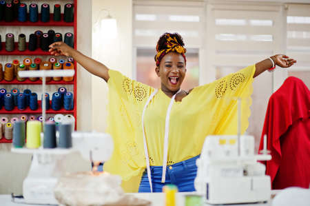 Young african dressmaker woman sews clothes on sewing machine at tailor office. Black seamstress women.の写真素材