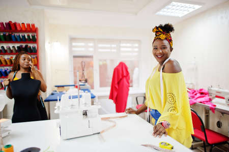 Two african dressmaker woman sews clothes on sewing machine at tailor office. Black seamstress girls.の写真素材