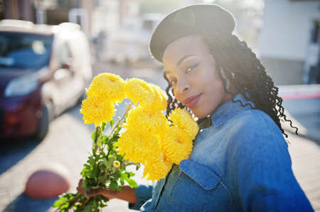 Stylish fashionable african american women in jeans wear and black beret with yellow flowers bouquet...