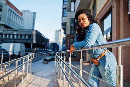 Stylish fashionable african american women in jeans wear and black beret against modern building.の写真素材