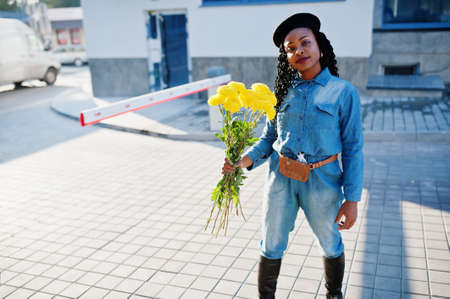 Stylish fashionable african american women in jeans wear and black beret with yellow flowers bouquet...