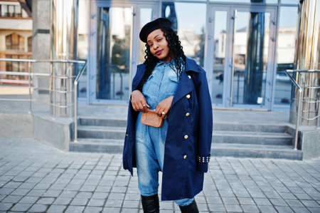 Stylish fashionable african american women in jeans wear and black beret with blue coat against...