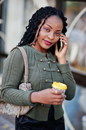 Stylish fashionable african american women in green sweater and black skirt posed outdoor cafe with...