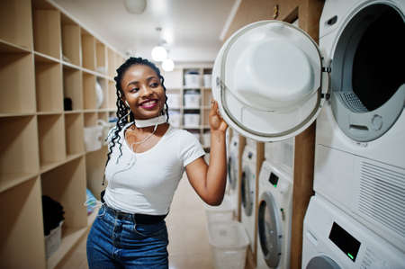Cheerful african american woman near washing machine in the self-service laundry.の写真素材