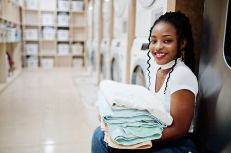 Cheerful african american woman with towels in hands near washing machine in the self-service laundry.の素材 [FY310159709020]