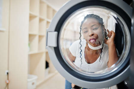 Funny portrait of cheerful african american woman near washing machine in the self-service laundry.の写真素材