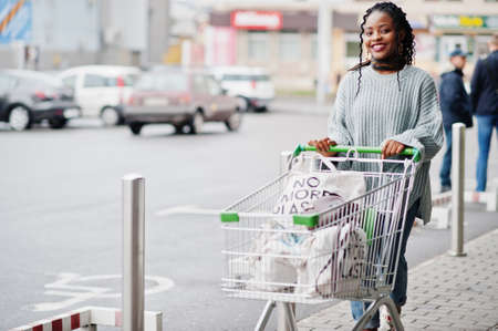 African woman with shopping cart trolley posed outdoor market near car parking.の写真素材