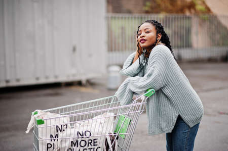 No more plastic. African woman with shopping cart trolley and eco bags posed outdoor market.