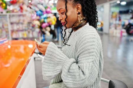 African woman bloger posed in sweater and jeans posed at mall with her mobile phone.
