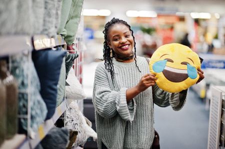 Face with tears of joy emoji. LOL concept. African woman with laughing out loud pillow in a modern home furnishings store.の写真素材