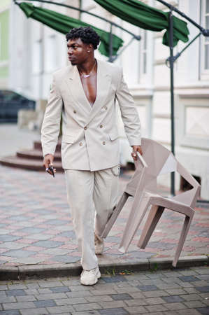 Stylish afro man in beige old school suit with mobile phone. Fashionable young African male in casual jacket on bare torso.の写真素材