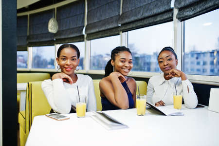 Three african woman in dress posing at restaurant, read the menu.