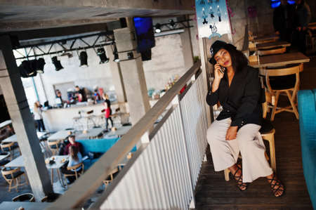Charming african american woman model in black jacket relaxing in cafe during free time with mobile phone.の写真素材